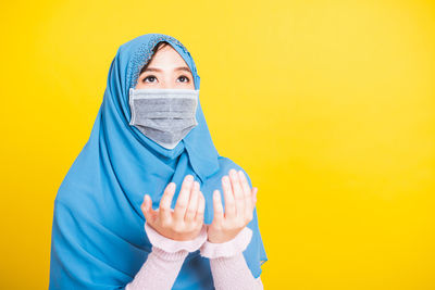 Portrait of woman covering face against yellow background