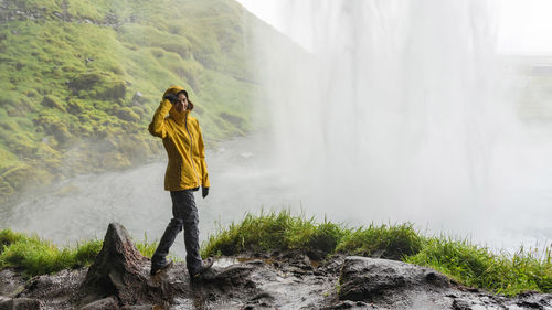 Happy female hiker in a bright rain coat behind powerful waterfall