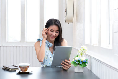Young woman using phone while sitting on table
