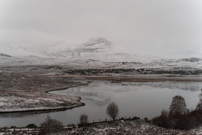 Scenic view of lake by snowcapped mountain against sky