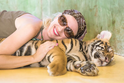 Close-up of smiling young woman lying with tiger cub at zoo