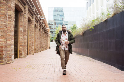 Bearded man walking across pathway holding a take away coffee