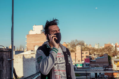 Young man with face mask standing against sky in city