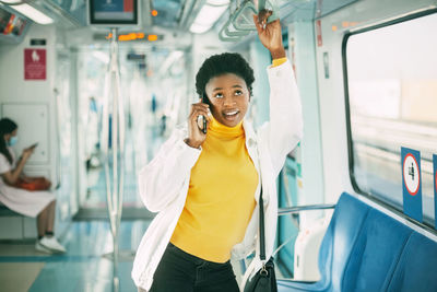 Portrait of smiling young man holding mobile phone while standing in bus