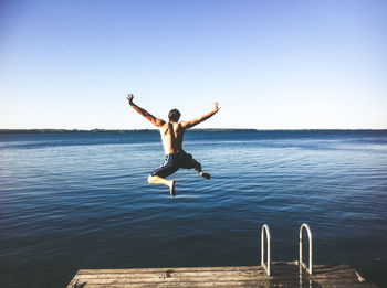 Full length of shirtless man jumping in sea against clear sky