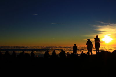 Silhouette people on beach against sky during sunset