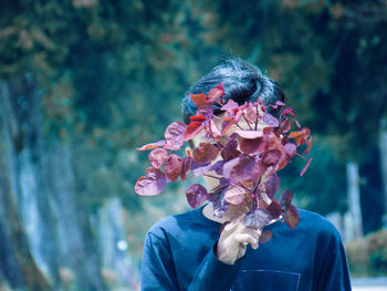 Portrait of teenage boy covering face with plant outdoors