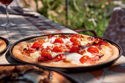 Homemade italian pizza with tomato, cheese and ham in the plate on tile table in the garden.