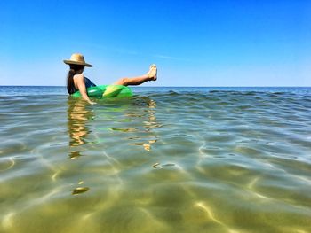 Woman relaxing in inflatable ring on sea against sky