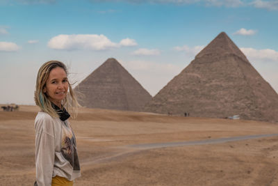 Portrait of woman standing in desert against pyramids and sky