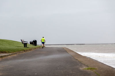 Rear view of men jogging on promenade against sky