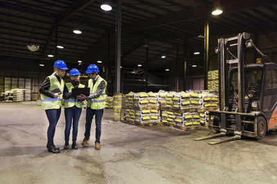 Full length of manual workers using laptop in cement warehouse