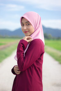Portrait of young woman in hijab standing on footpath against sky