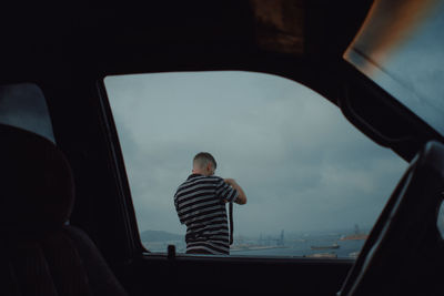 Rear view of man standing by car window