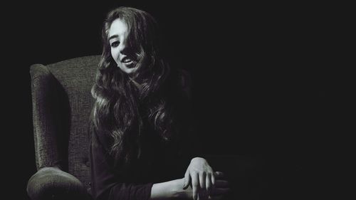 Portrait of woman sitting against black background