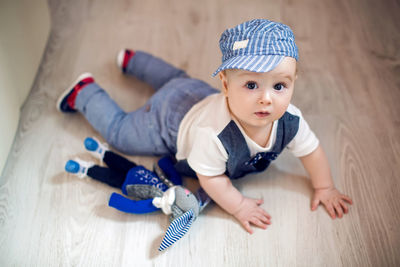 Gay boy kid blonde in a cap and pants lying on the floor next to a toy rabbit