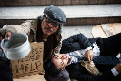 Portrait of beggar asking for help while drunk businessman lying on roadside