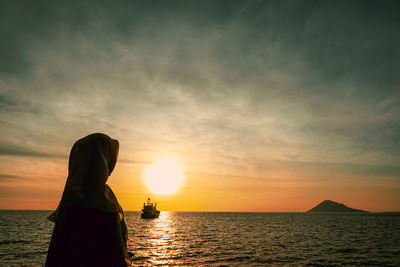 Silhouette people on sea against sky during sunset