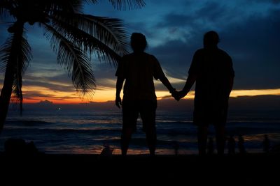 Silhouette couple standing at beach against cloudy sky