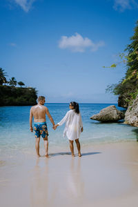 Rear view of friends on beach against sky