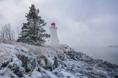 Lighthouse on snow covered field against sky