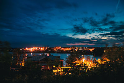 Illuminated buildings by lake against sky at night