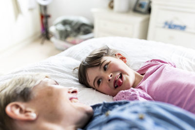 Girl sticking out tongue and lying down by mother in bedroom