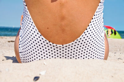 Rear view of woman siting on sand at beach against sky