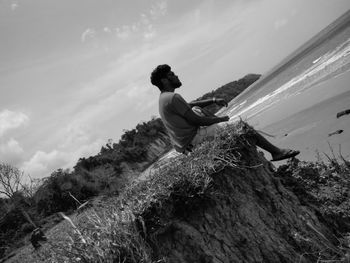 Young man sitting on cliff at beach