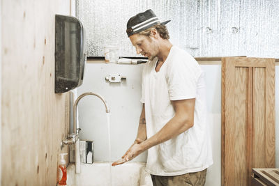 Side view of a man standing against wall at home