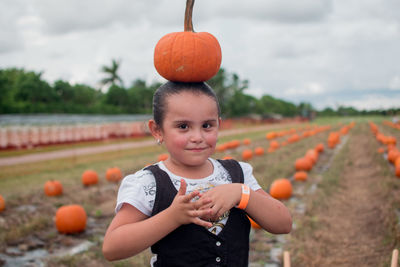 Portrait of cute girl balancing pumpkin on head while standing at field