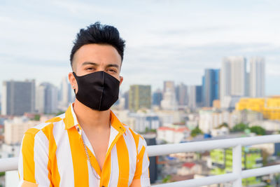 Portrait of young man standing against buildings in city