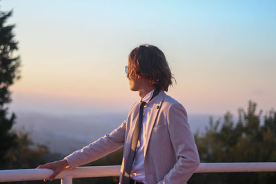 Portrait of young long-haired man in an elegant blush suit outfit looking at the endless landscape 