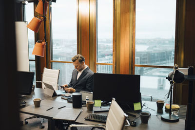 Mature businessman using smart phone at table in board room