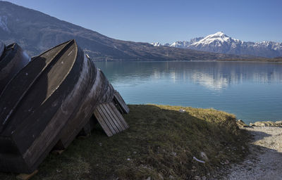 Old boats moored at lakeshore by mountains against clear sky
