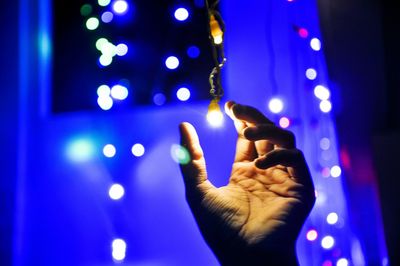 Low angle view of hand against illuminated light at night