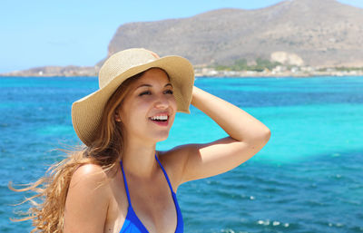 View of smiling young woman in hat against sea