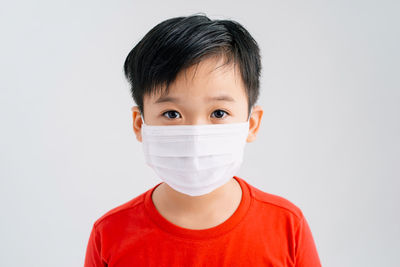 Portrait of boy wearing pollution mask standing against white background