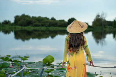 Rear view of woman standing by lake against sky