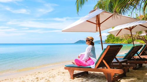 Woman sitting on beach against sky