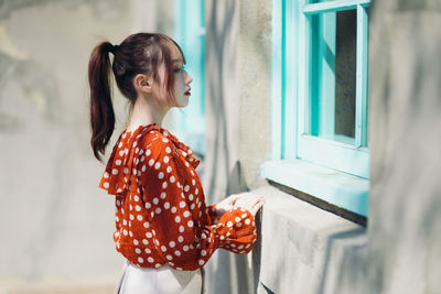 Side view of young woman standing by window
