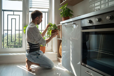 Young man wearing back support belt taking care of houseplants at home