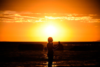 Silhouette woman standing on beach against orange sky