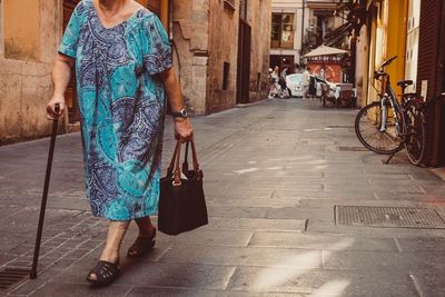 Low section of senior woman walking on footpath in city