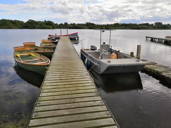 Boats moored on pier at lake against sky