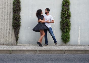 Full length portrait of young couple dancing against wall