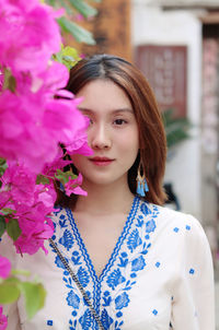 Portrait of beautiful young woman standing by pink flowering plants