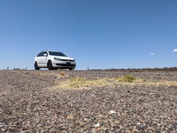 Car on road by land against clear blue sky