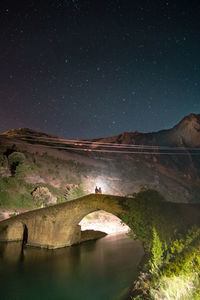 Couple standing on arch bridge over river at night