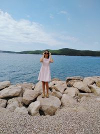 Woman standing on rock by sea against sky